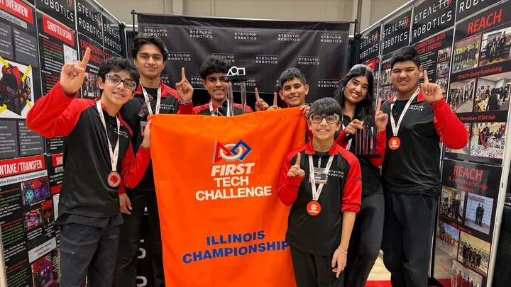 Image of the Stealth Robitcs team posing with their Illinois Championship Flag for the First Tech Challenge.